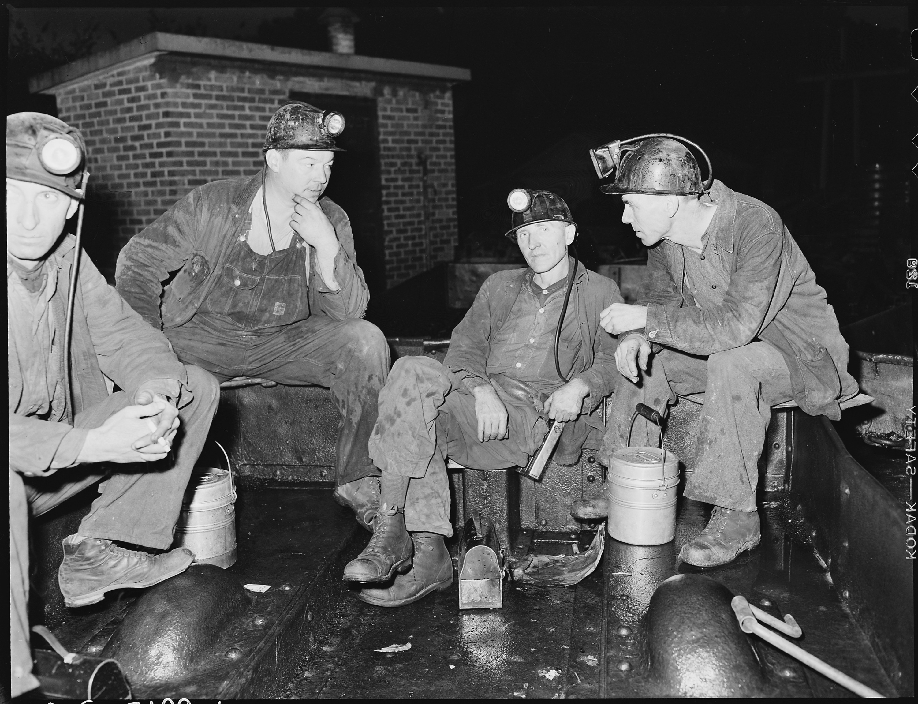 Grupa górników w hełmach z lampami czeka na zjazd do kopalni przed poranną szychtą (fot. Russell Lee, 1946).