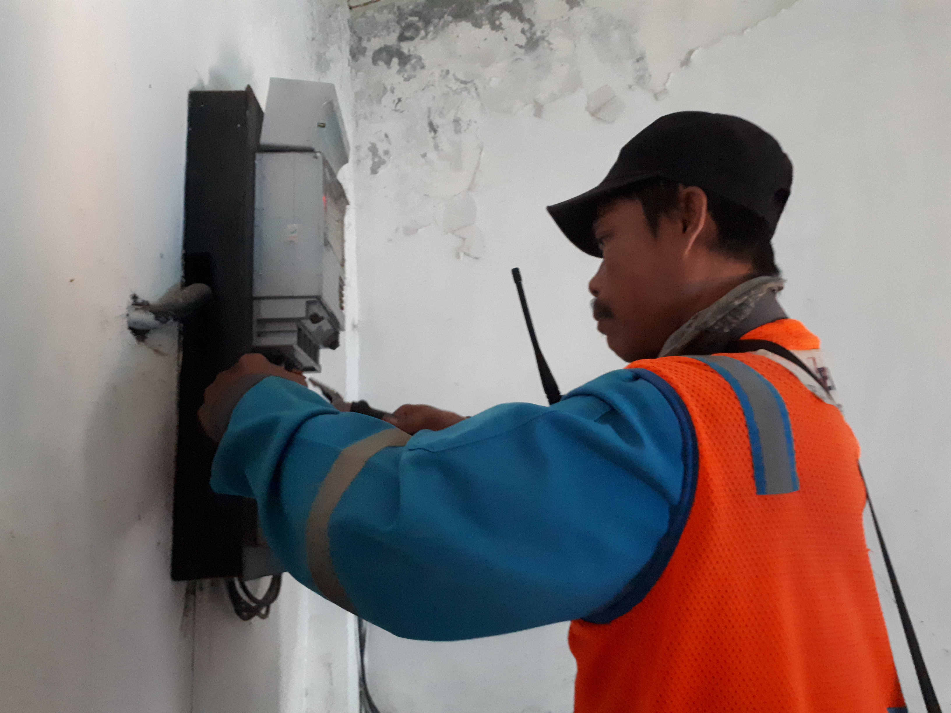 Elektryk w kamizelce odblaskowej pracuje przy liczniku energii elektrycznej na ścianie budynku.